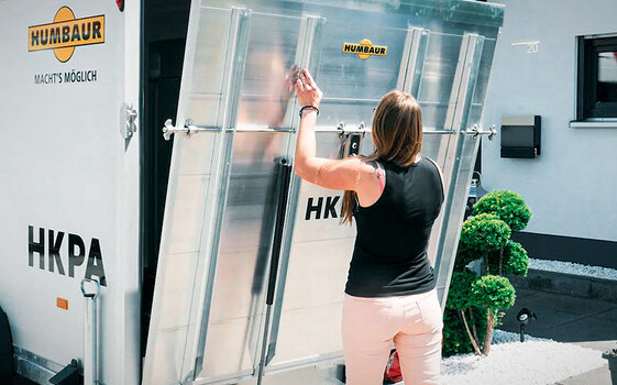 Heckklappe öffnen | © Humbaur GmbH Eine Frau öffnet die Heckklappe eines HKPA Kofferanhängers von Humbaur | © Humbaur GmbH