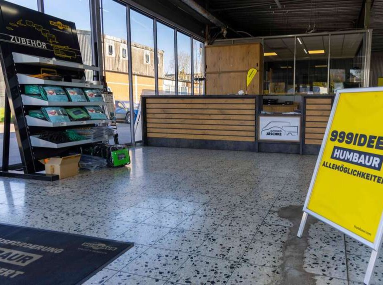 Moderner Eingangsbereich vom Autohaus Jäschke mit Humbaur Ersatzteilregal links und Willkommens Schild rechts daneben.